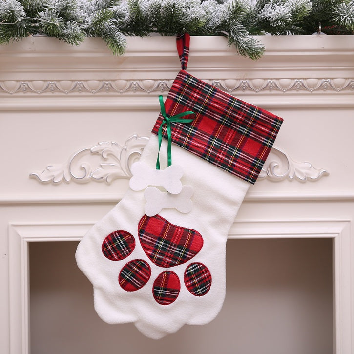 White Christmas stocking with red plaid paw prints hanging on a fireplace mantle.